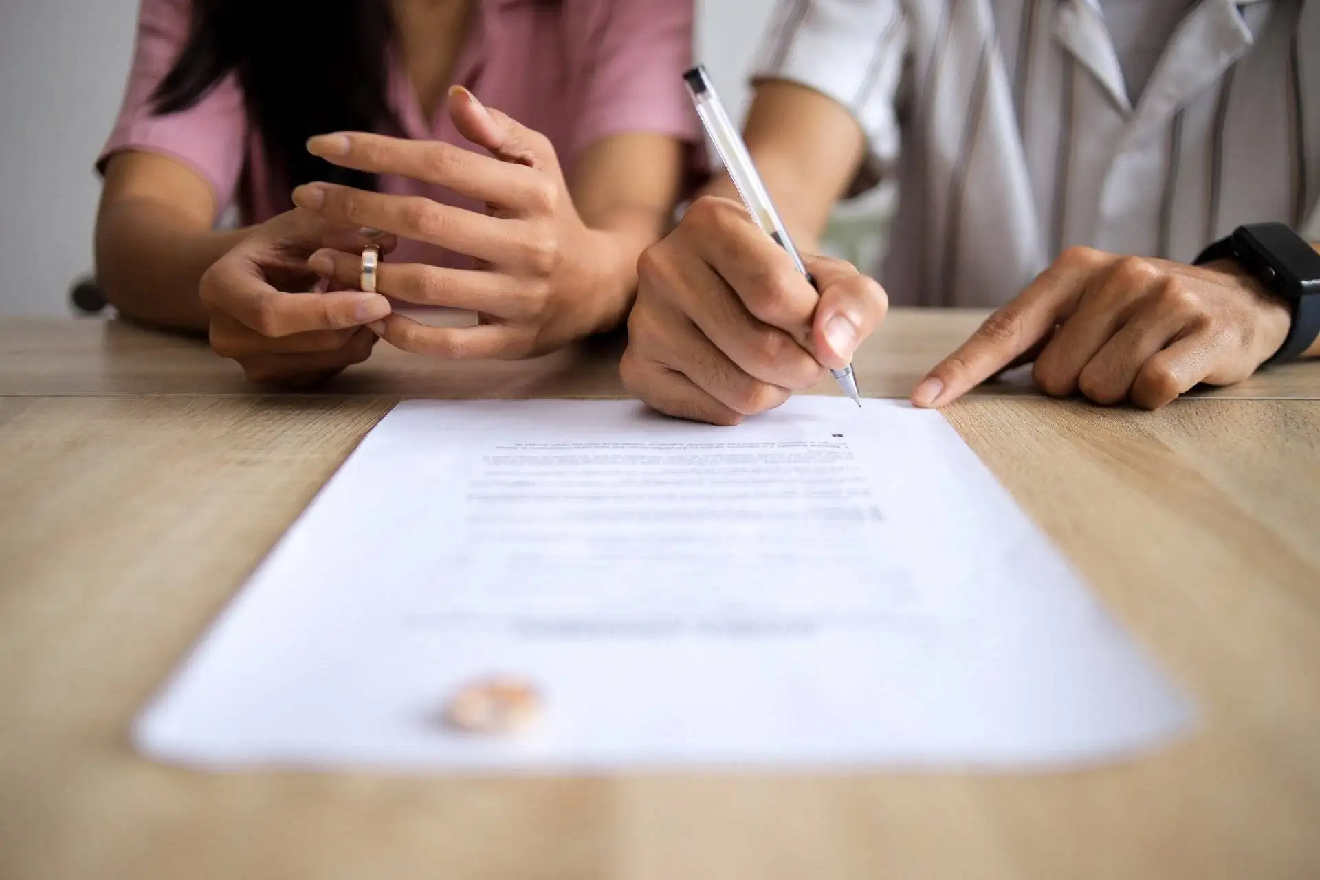 Couple signing divorce documents at a wooden table