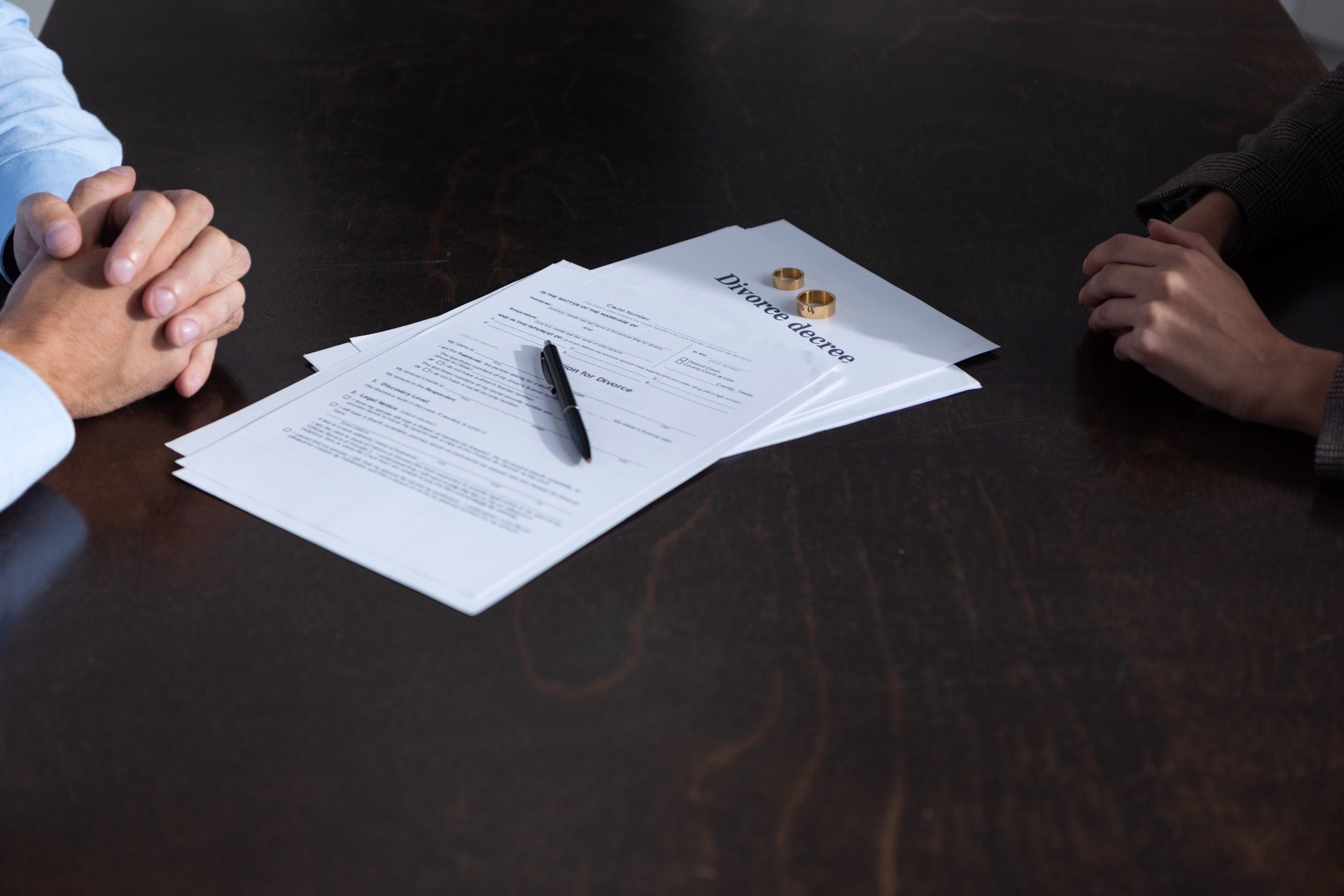Divorce papers and wedding rings on a table between a couple