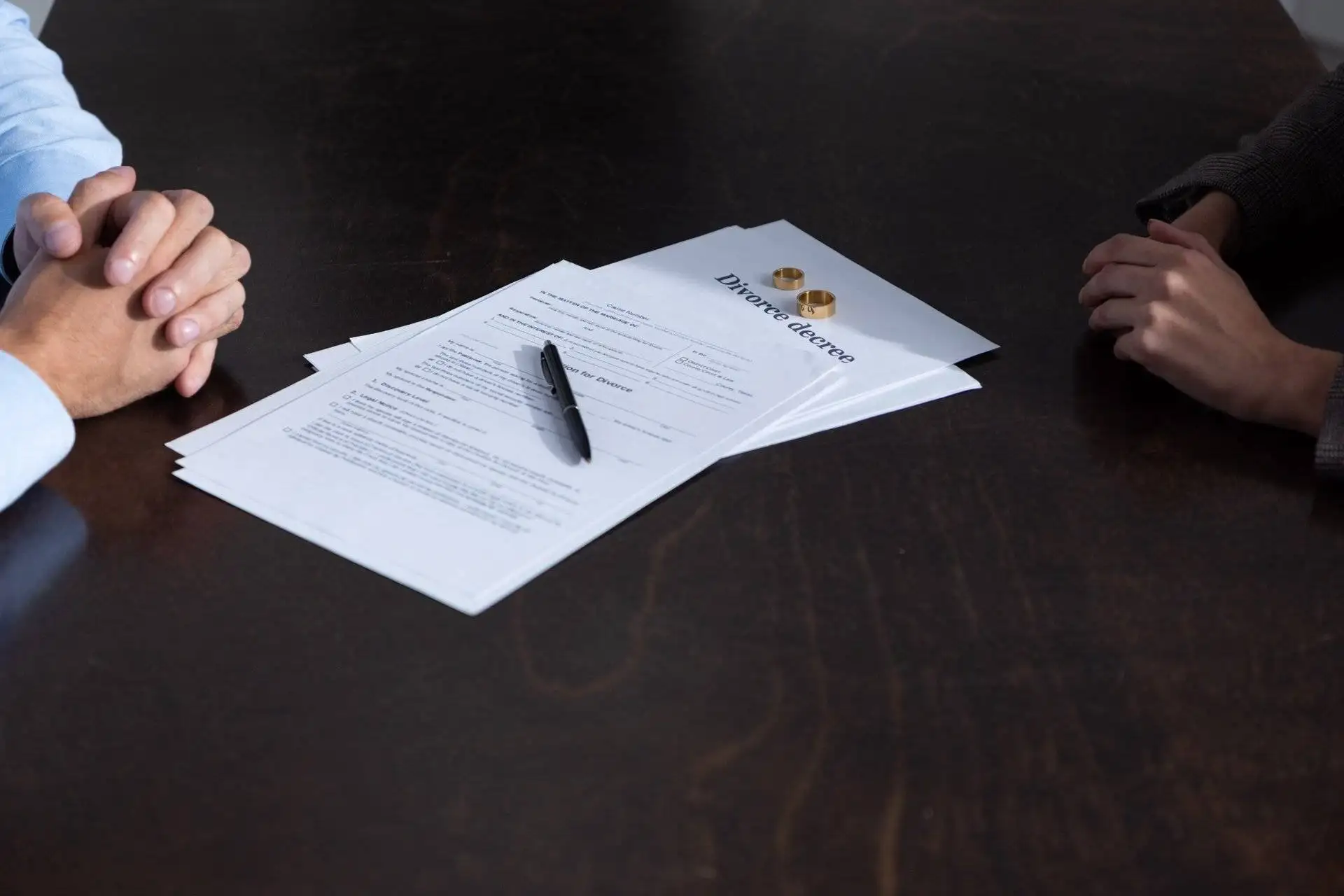Divorce papers and wedding rings on a table between a couple
