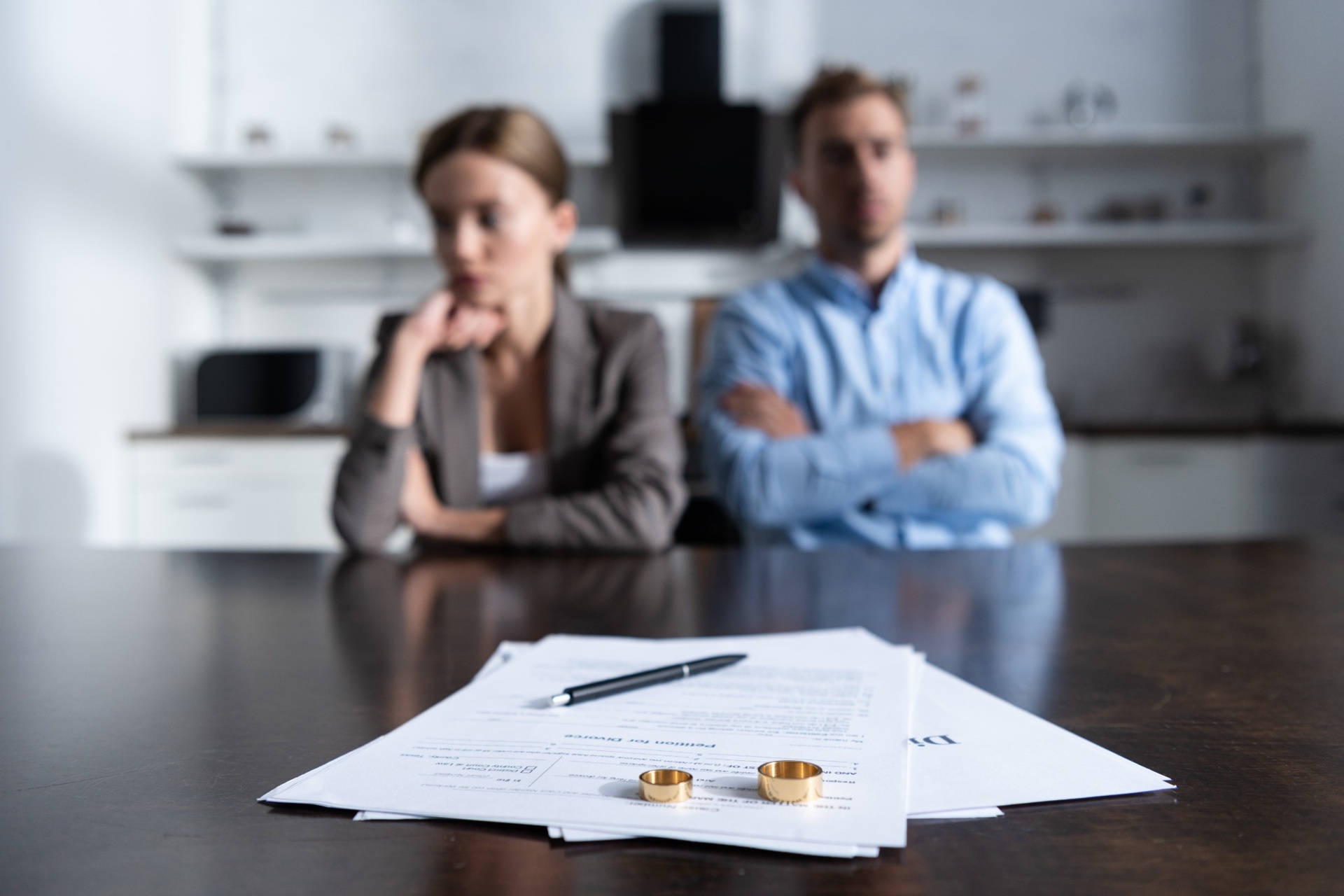 Divorce paperwork and wedding rings on table with couple arguing in background