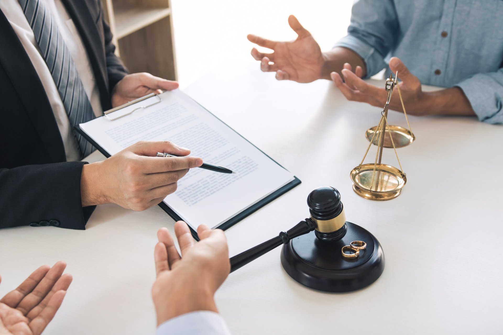 Divorcing couple discussing legal matters with wedding rings and gavel on table