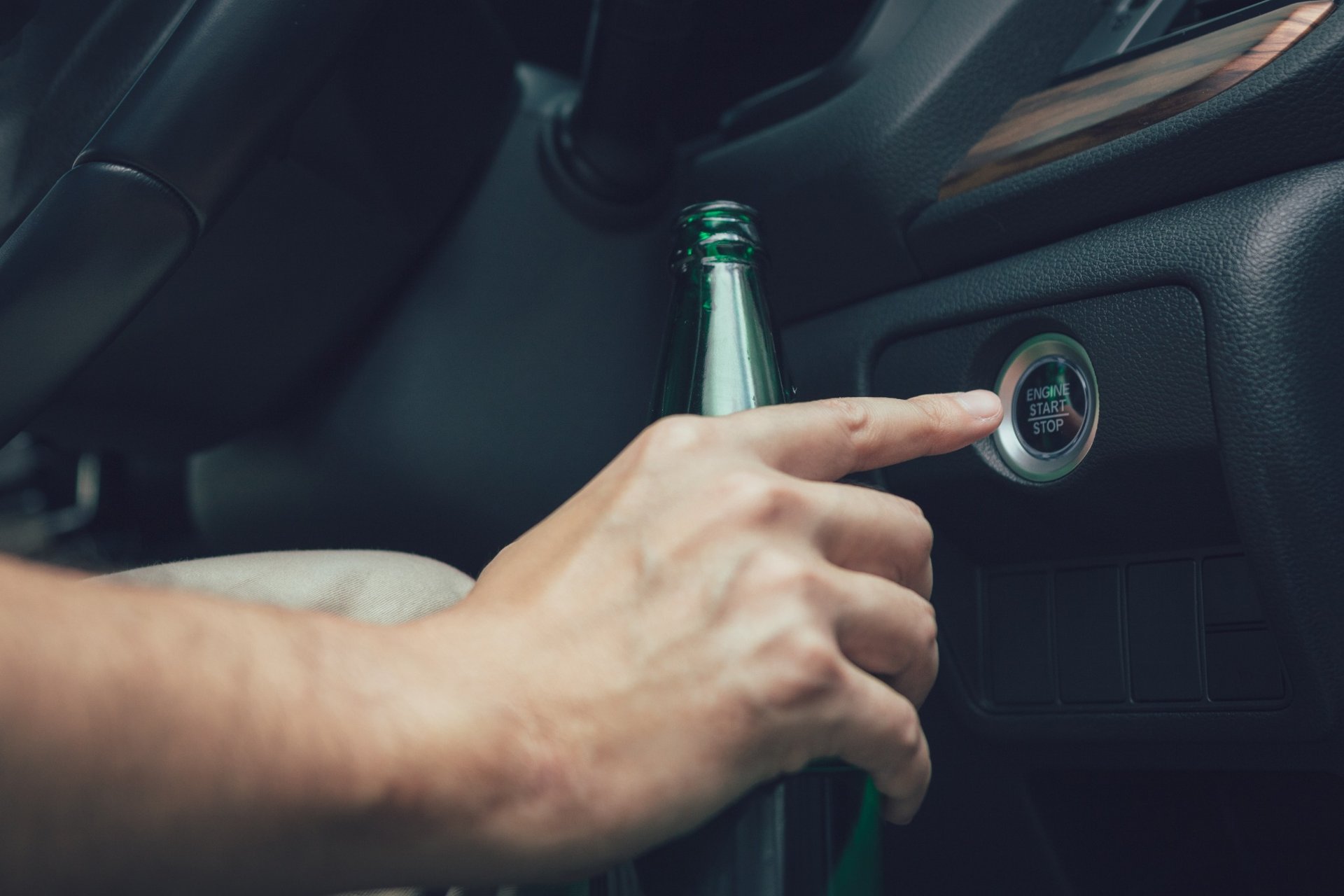 Driver holding a beer bottle while pressing a car’s engine start button