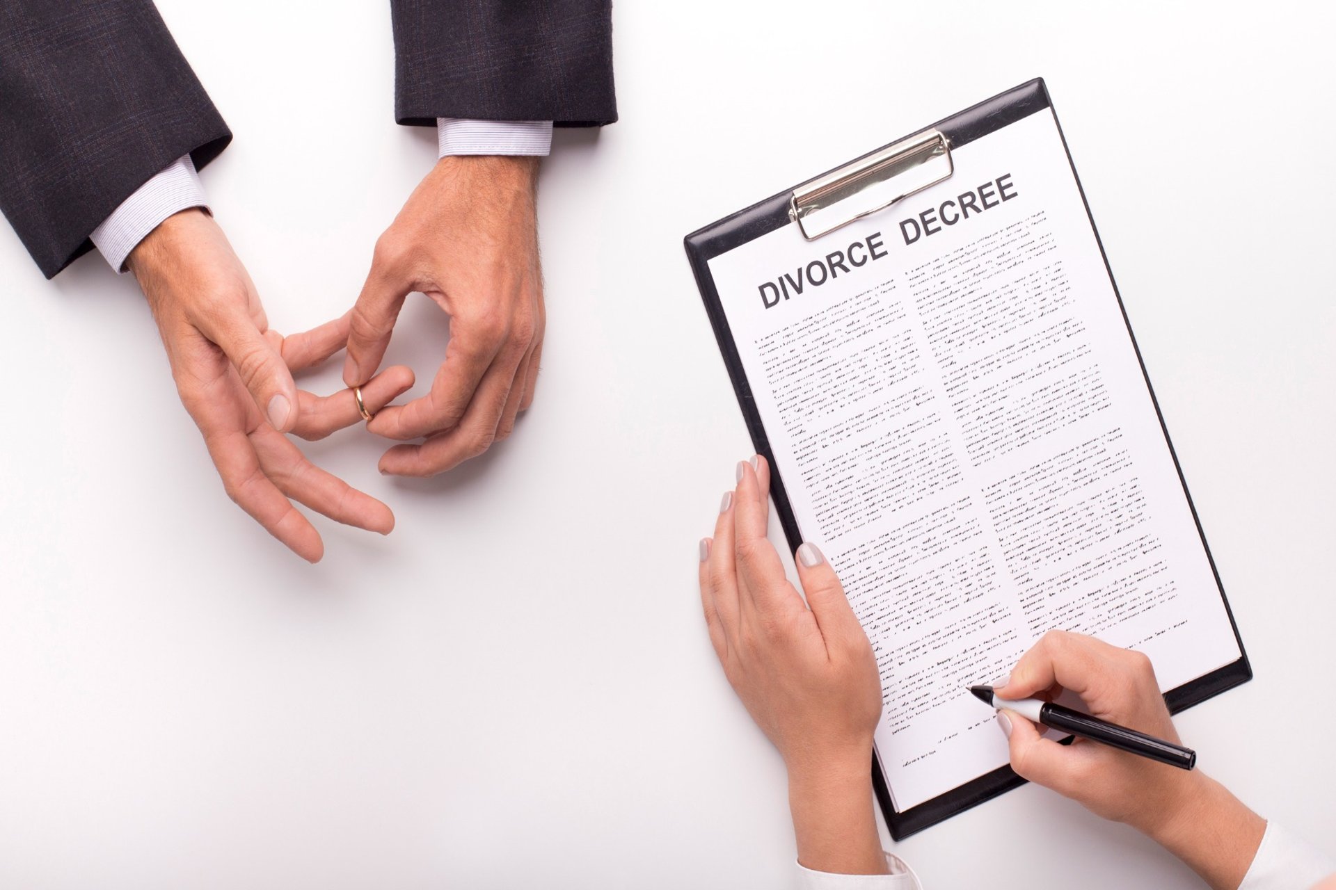 Man removing wedding ring next to divorce decree paperwork