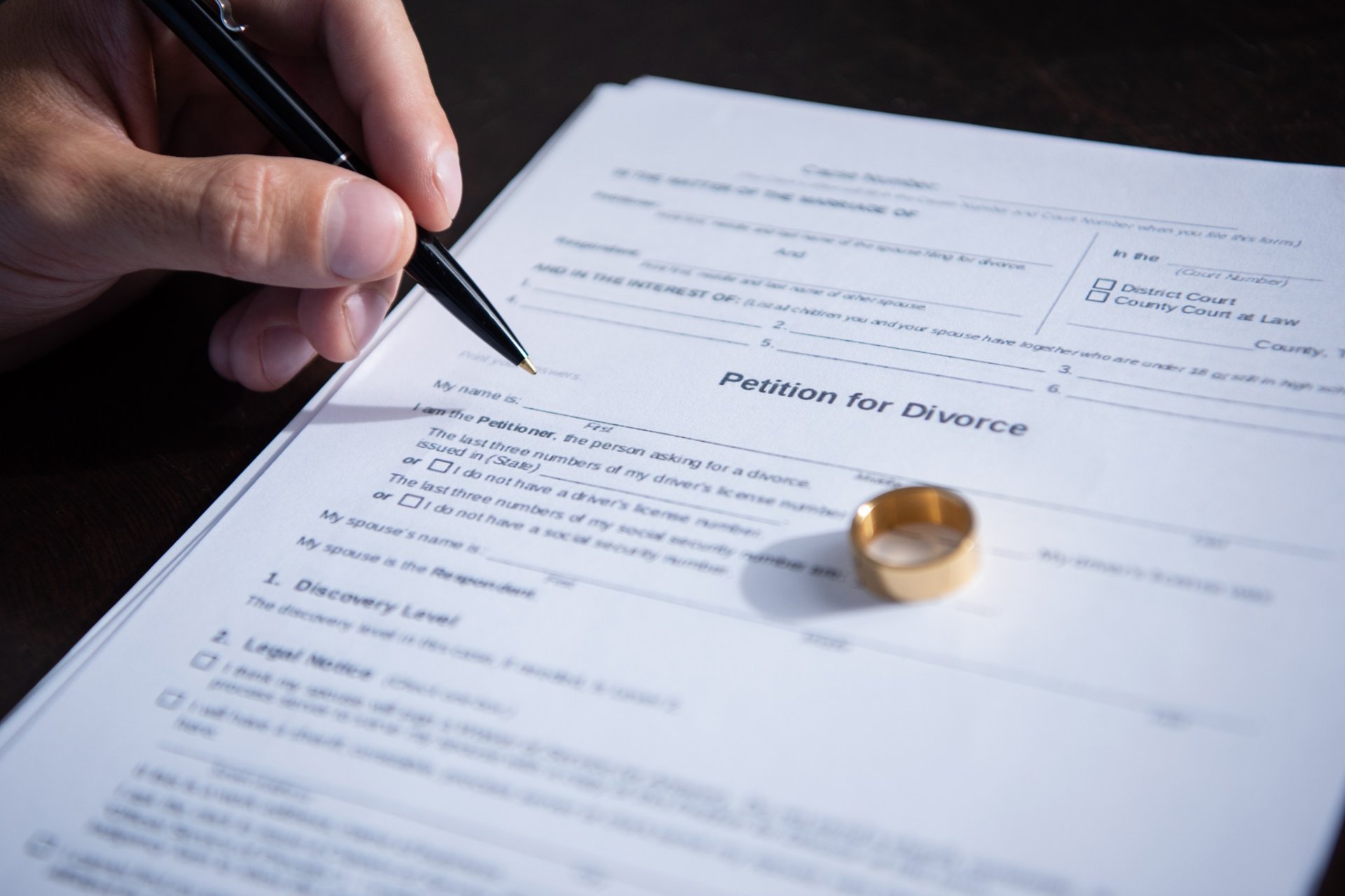 Man signing petition for divorce with wedding ring beside document