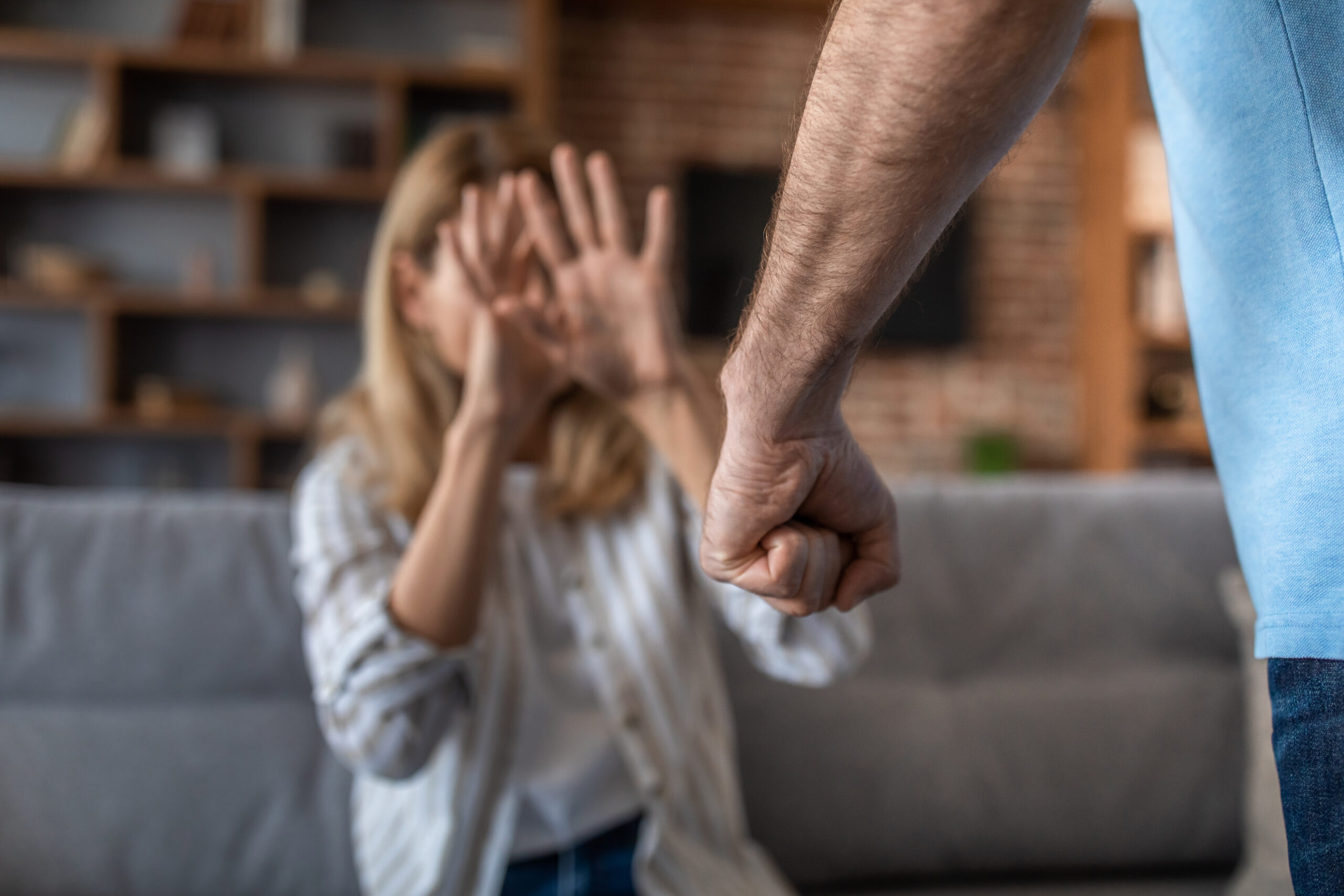 Sad crying adult wife covers her face, afraid of her aggressive husband in living room