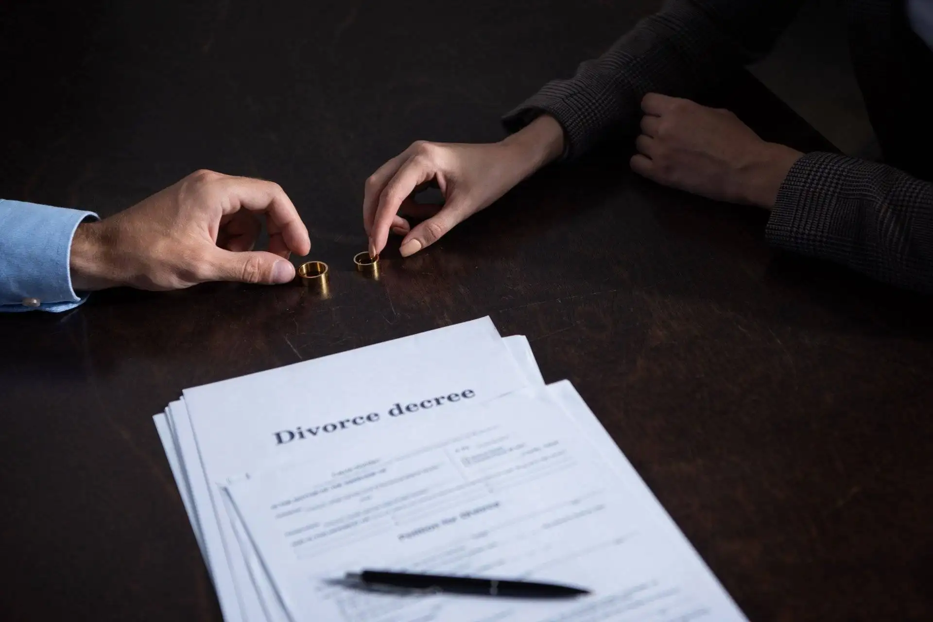 Two people at a table exchanging wedding rings next to divorce papers
