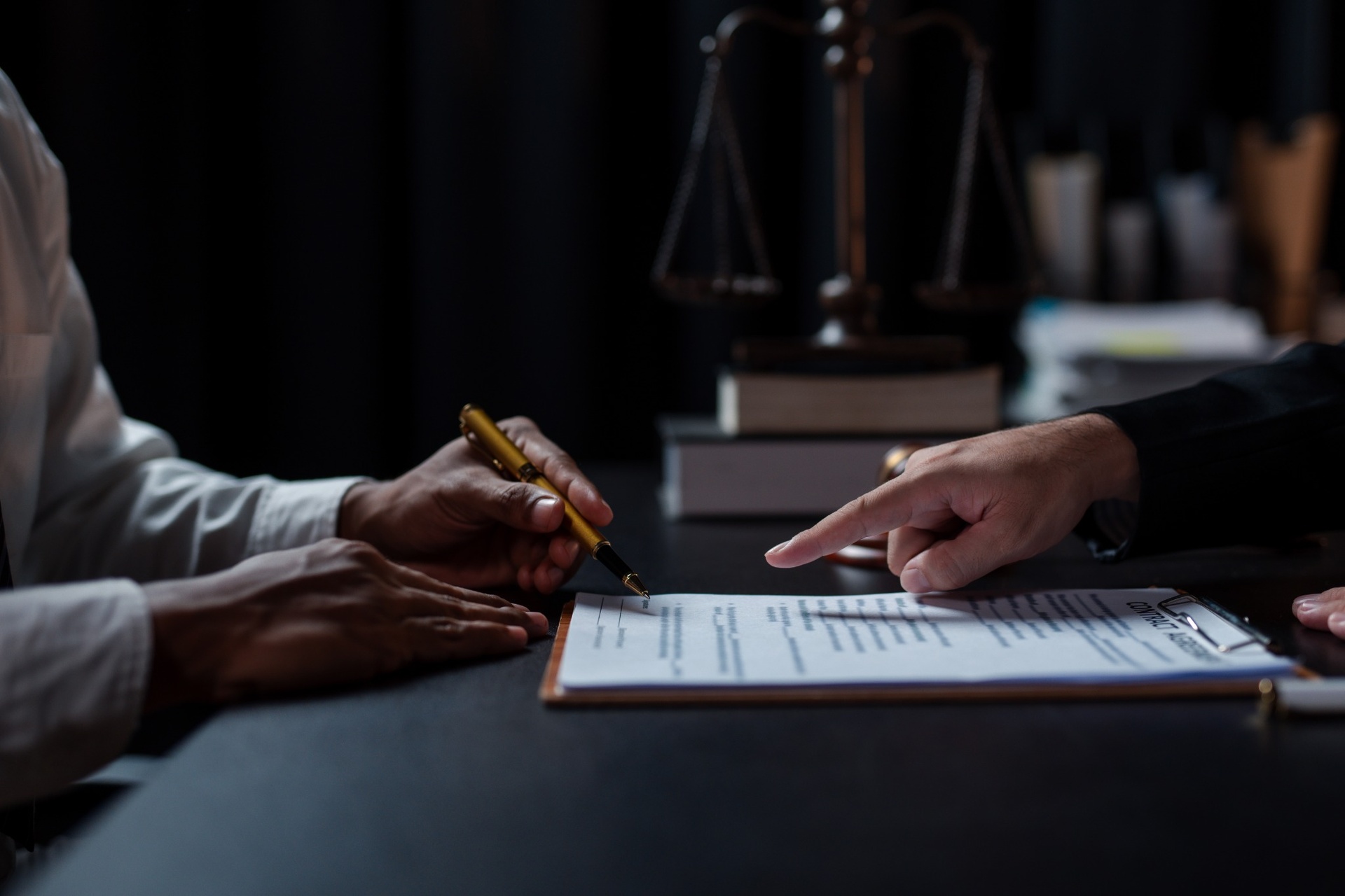 Close-up of two people discussing and signing a legal document with a justice scale in the background