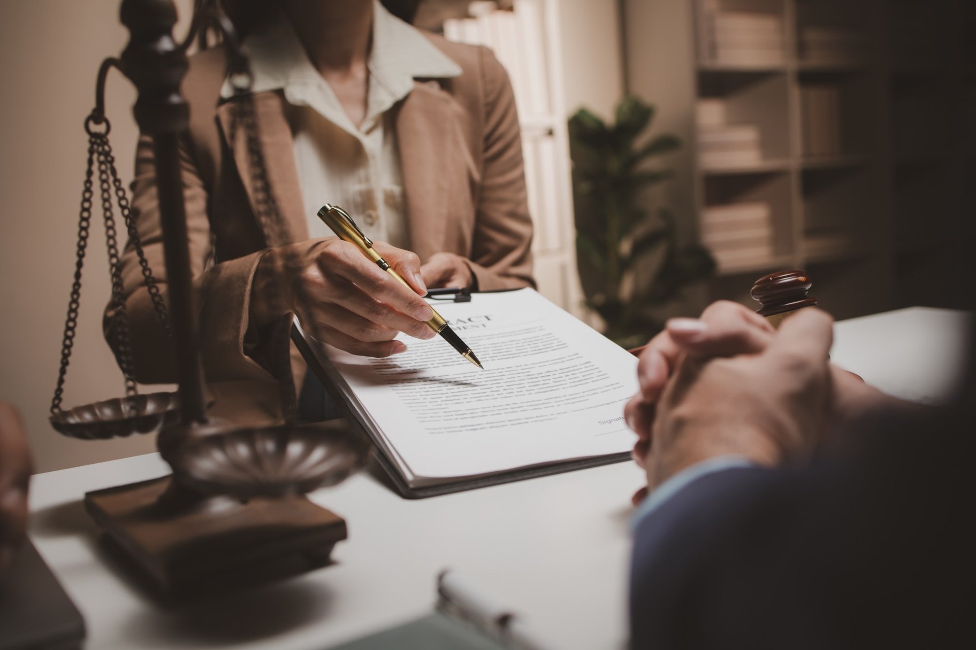 Lawyer showing client where to sign legal contract with scales of justice in foreground
