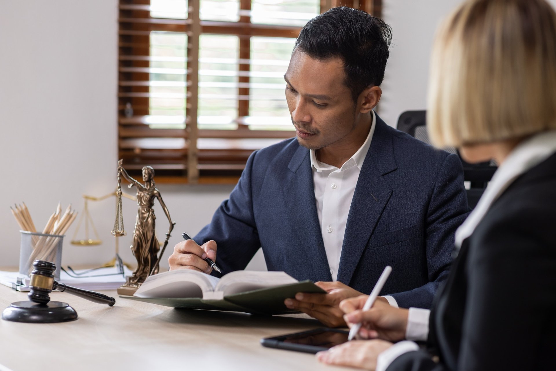 Male attorney writing notes while consulting with female colleague in law office