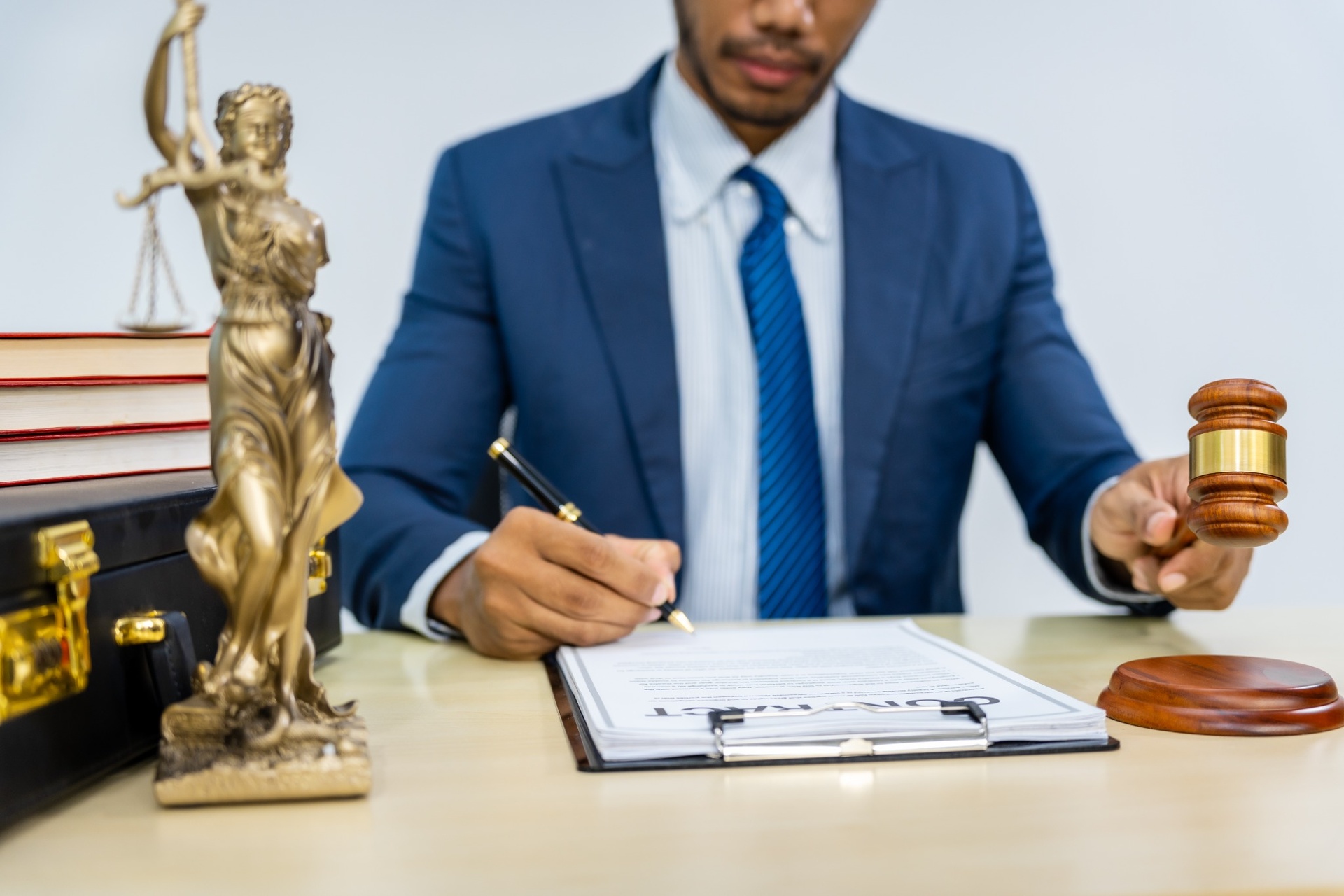 Male lawyer in a suit signing a contract with a gavel and Lady Justice statue on the desk