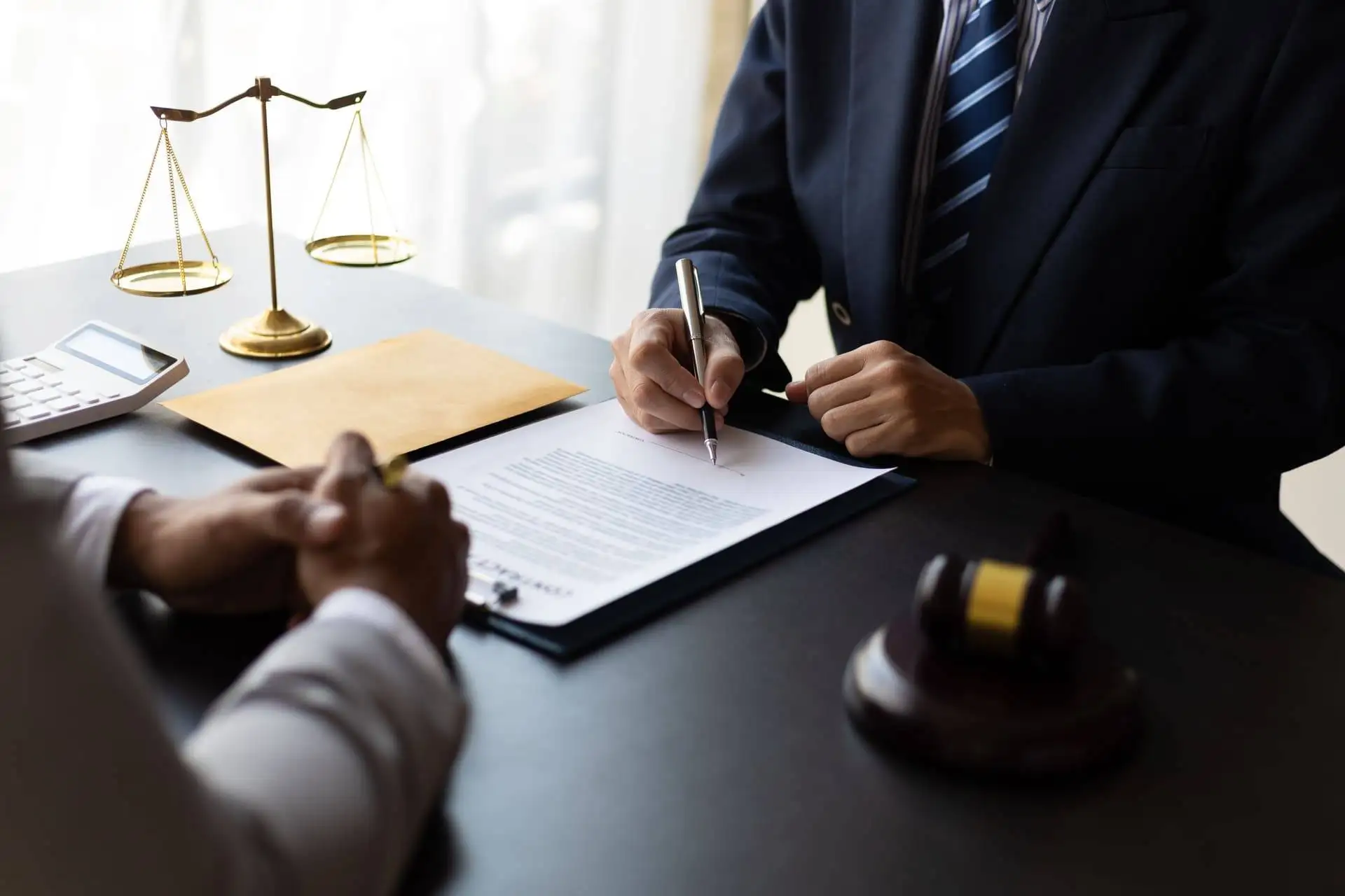 Lawyer signing legal documents at a desk with scales of justice and a gavel