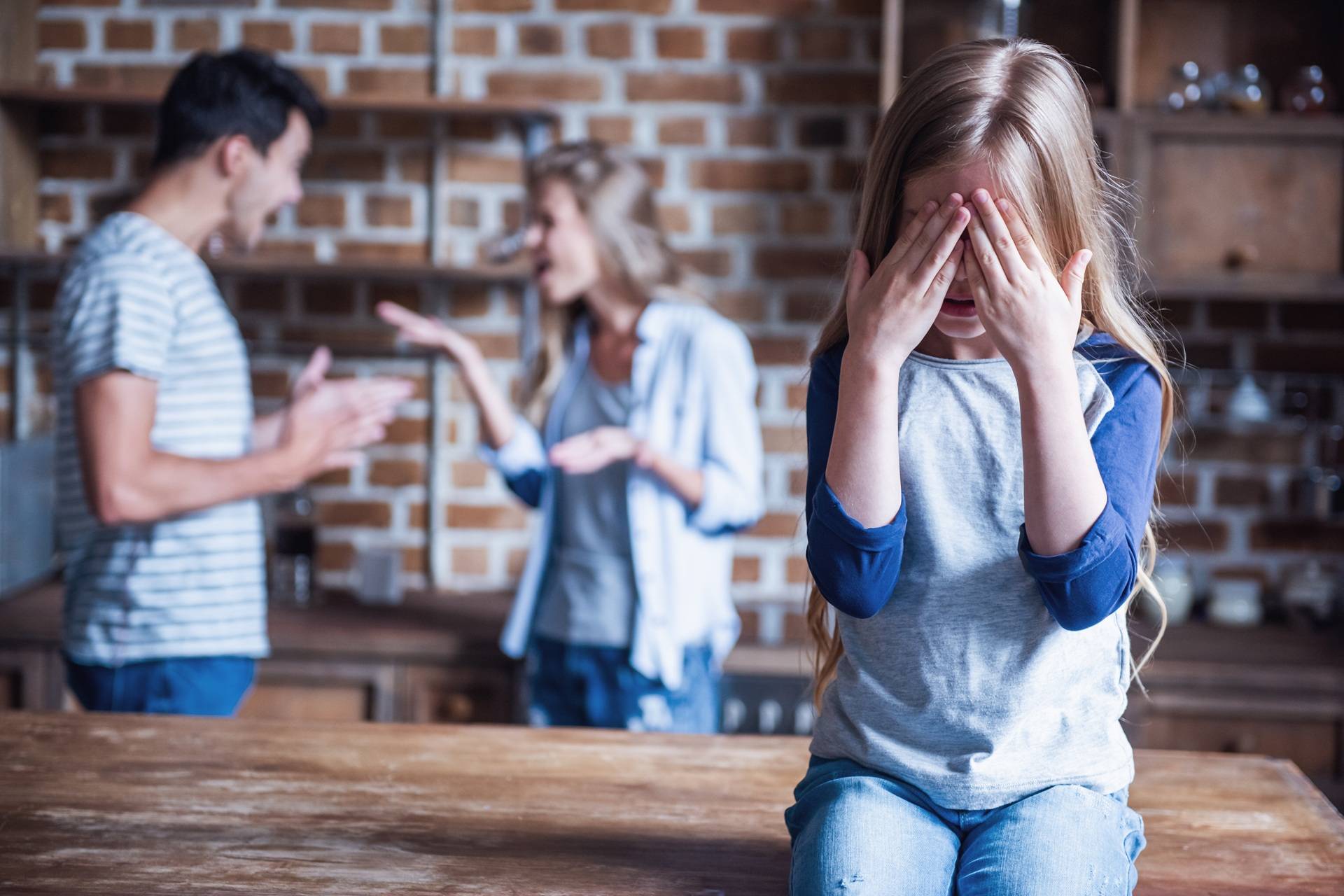 Little girl is crying while her parents are arguing in the background in kitchen