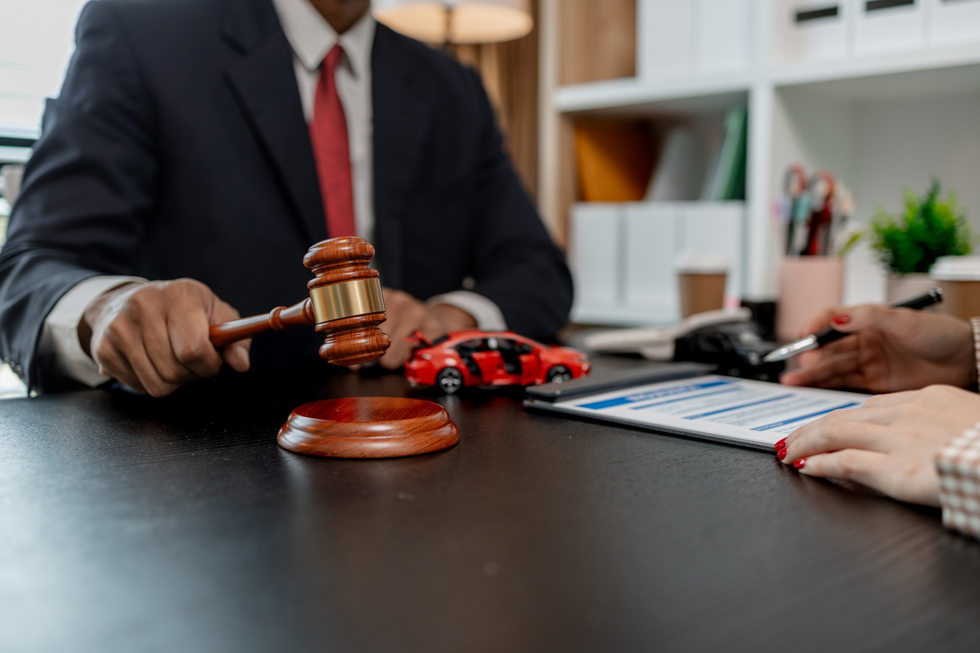 Close-up of a lawyer in a suit holding a gavel next to toy cars and legal documents during a car accident consultation
