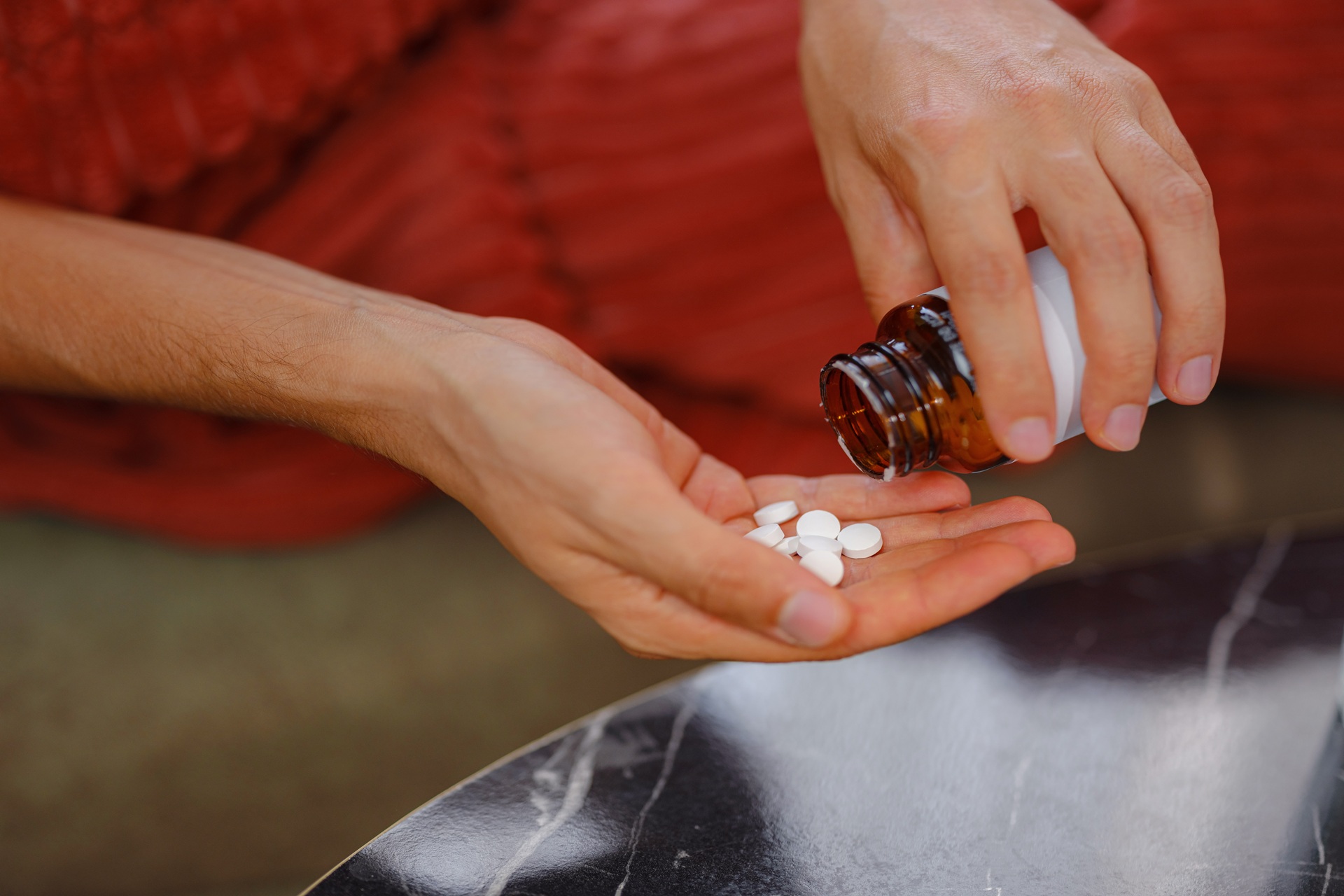 Person pouring white tablets from an amber prescription bottle into their hand while sitting indoors