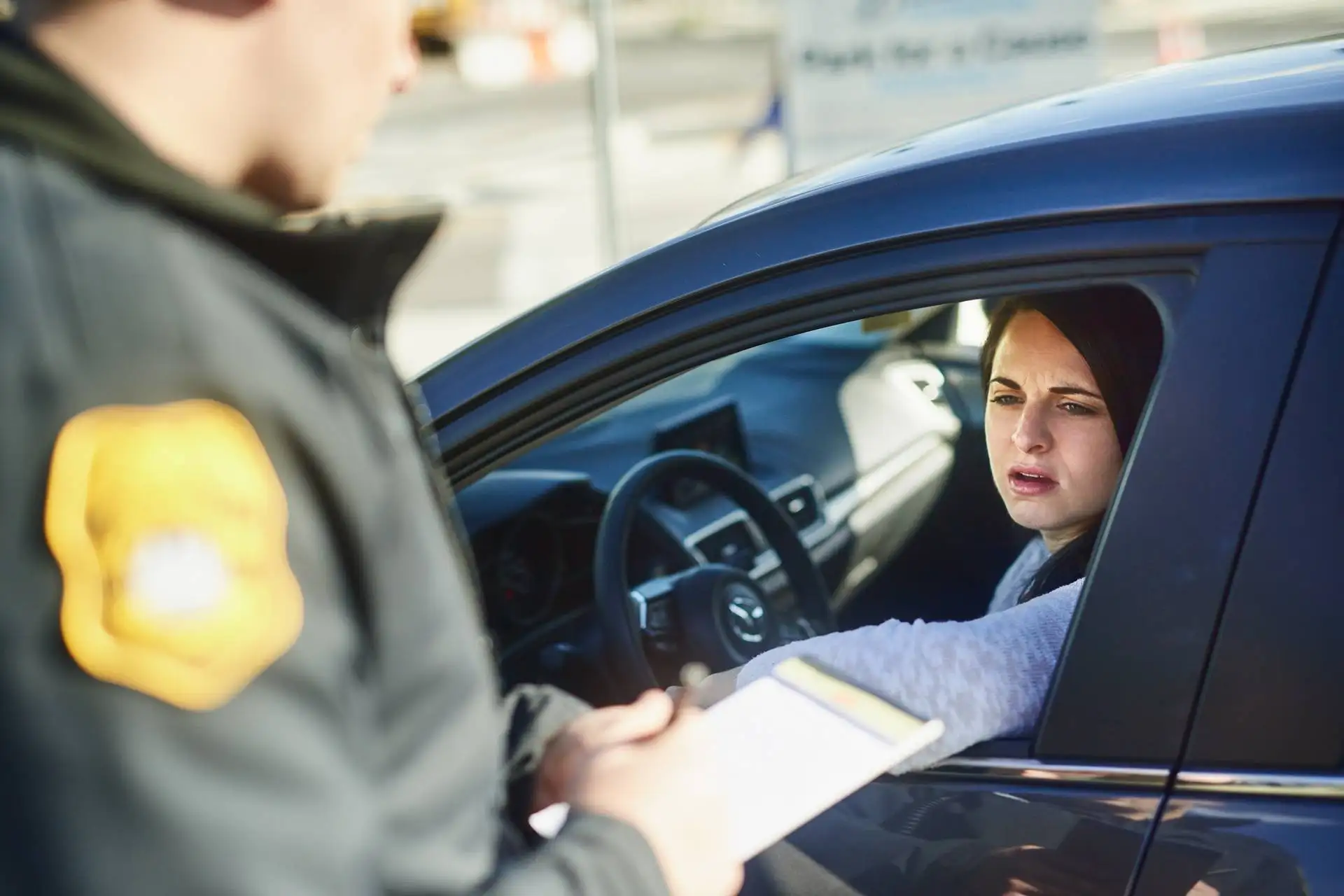 Policeman writing a ticket while a concerned female driver leans out of her car window, resting her head on her hand
